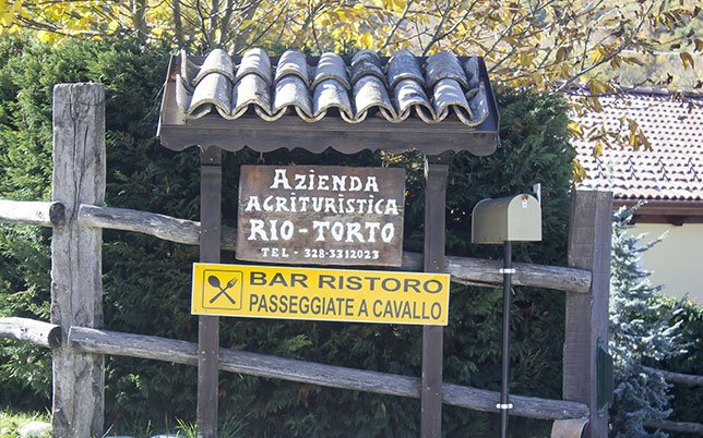 agriturismo-rio-torto-foto-chi-siamo-1 Insegna in legno dell’Agriturismo Rio Torto: simbolo di gestione familiare agriturismo, dove ogni dettaglio racconta passione, accoglienza e legame con il territorio.